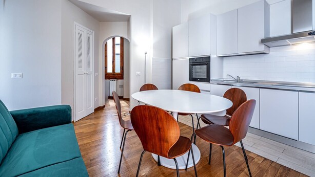 A modern kitchen with white cabinets, a round dining table, and wooden chairs. - Poggi 22 (Florence)