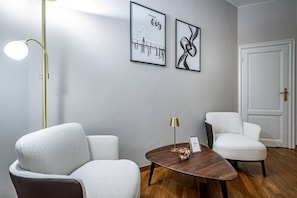 A modern room with two white armchairs, a wooden coffee table, a gold floor lamp, and two framed artworks on the wall. - Poggi 22 (Florence)