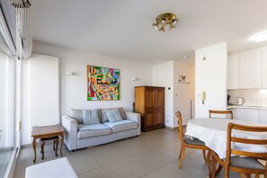 Ein Wohnzimmer mit Sofa, einem Holztisch, einem Esstisch mit Stühlen, einer Küchenzeile und einem farbenfrohen, abstrakten Gemälde an der Wand.