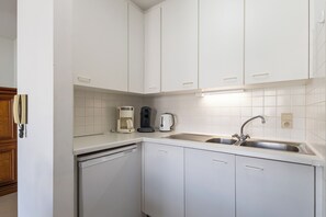 A modern kitchen with white cabinets, a dishwasher, a coffee maker, and a sink. - Ravelingen 0101+ G * (Koksijde)