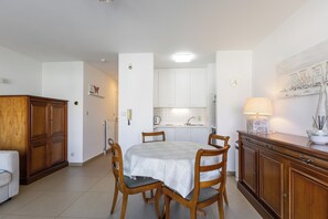 A dining area with a table, chairs, a cabinet, and a kitchen in the background. - Ravelingen 0101+ G * (Koksijde)