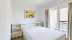Ein Schlafzimmer mit einem Bett, einem Nachttisch, einem Regal, einem Fenster mit Vorhängen und einem Bild an der Wand.