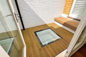 A modern room with a glass door, a wooden floor, a white brick wall, and a small wooden bench. - Kensington House-3 Mins Walk to Hyde Park (London)
