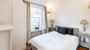 Ein Schlafzimmer mit einem Bett, Nachttischen, einem Fenster mit Vorhängen und einer Heizung.