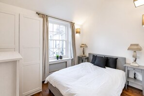 Ein Schlafzimmer mit einem Bett, Nachttischen, einem Fenster mit Vorhängen und einer Heizung.