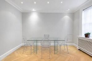 Une salle à manger moderne avec une table et des chaises en verre, des murs blancs et un plancher en bois.