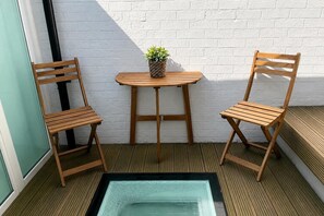 Ein kleiner Außenbereich mit zwei Holzstühlen und einem Tisch, einer Topfpflanze und einem Glastisch auf einer Holzterrasse.