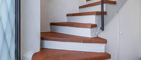 Un escalier aux murs blancs et aux marches marron, avec une main courante noire et un luminaire au-dessus.