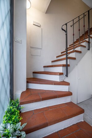 A staircase with white walls and brown steps, a black handrail, and a light fixture above. - Bolognese 4 (Florence)