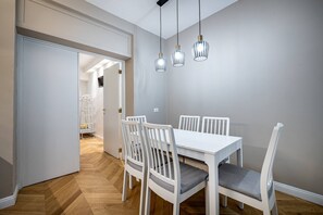 A dining area with a white table and chairs, three pendant lights, and a herringbone-patterned wooden floor. - Bolognese 4 (Florence)