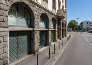 A building with arched windows and a green door, located on a street with parked cars and a clear sky. - Bolognese 4 (Florence)