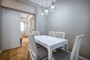 Un comedor con mesa y sillas blancas, suelo de madera y lámparas colgantes.
