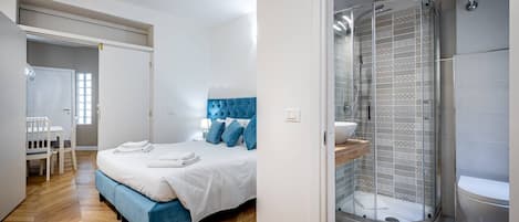 A modern bedroom with a bed, a blue headboard, a shower with a glass door, and a white sink.