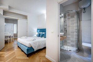 A modern bedroom with a bed, a blue headboard, a shower with a glass door, and a white sink. - Bolognese 4 (Florence)