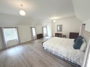 A bedroom with a large bed, a dresser, a nightstand, and a ceiling fan.