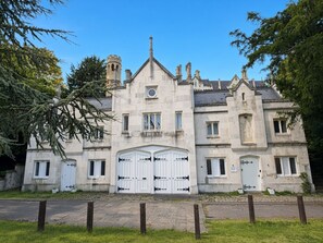 A historic stone building with a symmetrical facade, large white double doors, and a prominent tower with a clock.