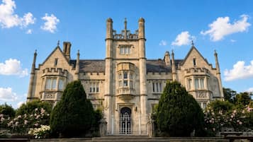 Un grand bâtiment historique à la façade symétrique, doté de nombreuses cheminées et d’une entrée centrale avec une porte grillagée.
