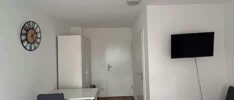 Une chambre d’hôtel avec deux lits, un bureau, une télévision, une horloge et une armoire.