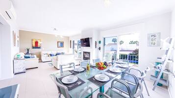 A modern living room with a dining area, white furniture, and a large window.
