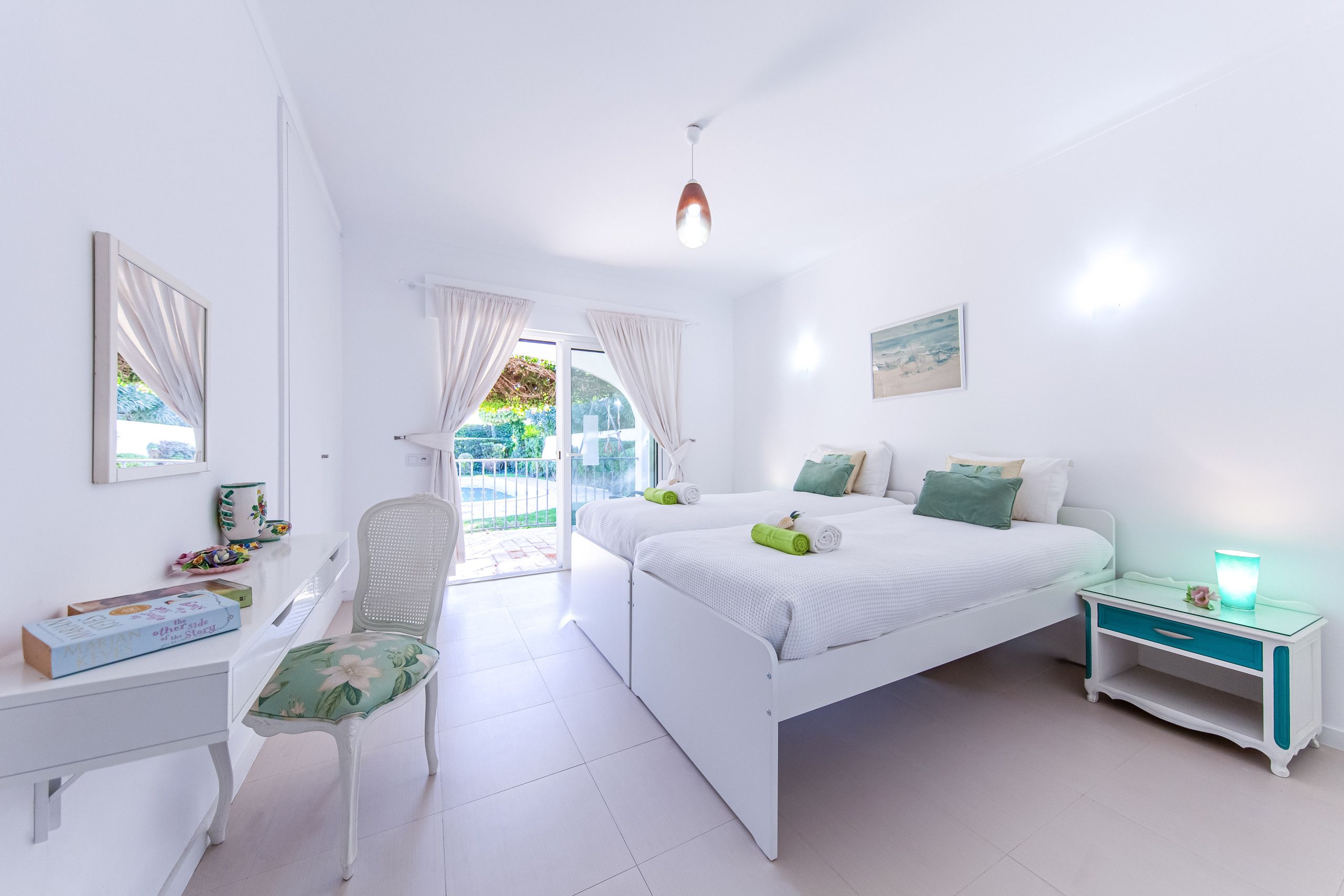 Una habitación luminosa y blanca con una cama, una silla, un escritorio y un ventanal.