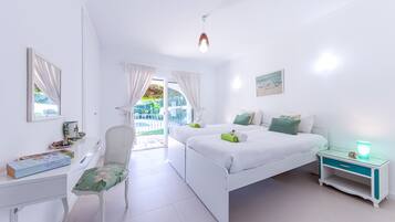 Una habitación luminosa y blanca con una cama, una silla, un escritorio y un ventanal.
