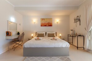 Ein modernes Schlafzimmer mit einem großen Bett, Nachttischen, einem Schreibtisch mit Stuhl und einem an der Wand befestigten Kunstwerk.