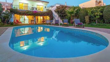 A swimming pool with lounge chairs, a staircase, and a building with balconies.