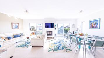 A modern living room with a sofa, a dining area with chairs and a table, and a TV on the wall.