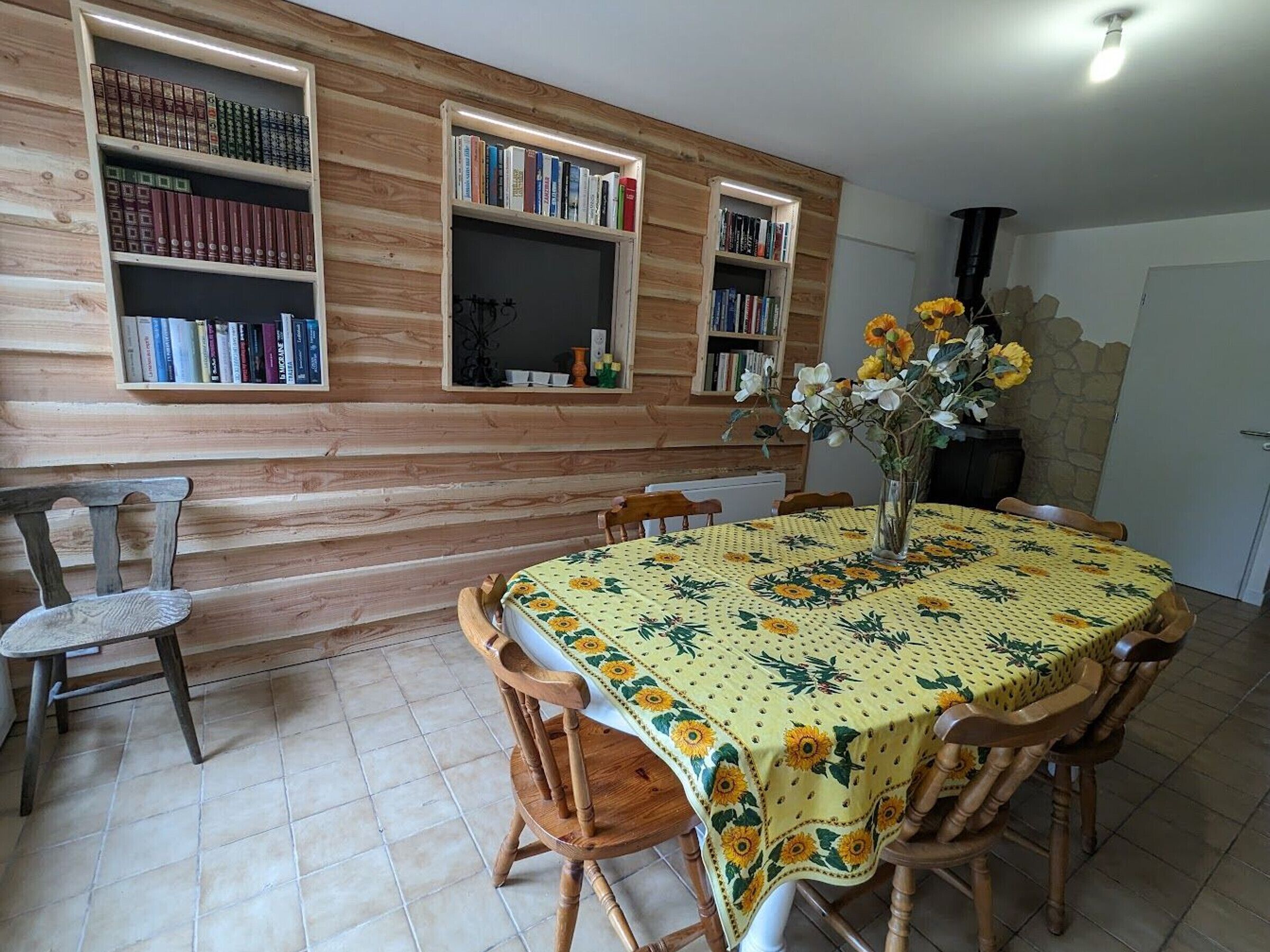 A dining area with a table covered by a floral tablecloth, surrounded by wooden chairs, and flanked by bookshelves filled with books.