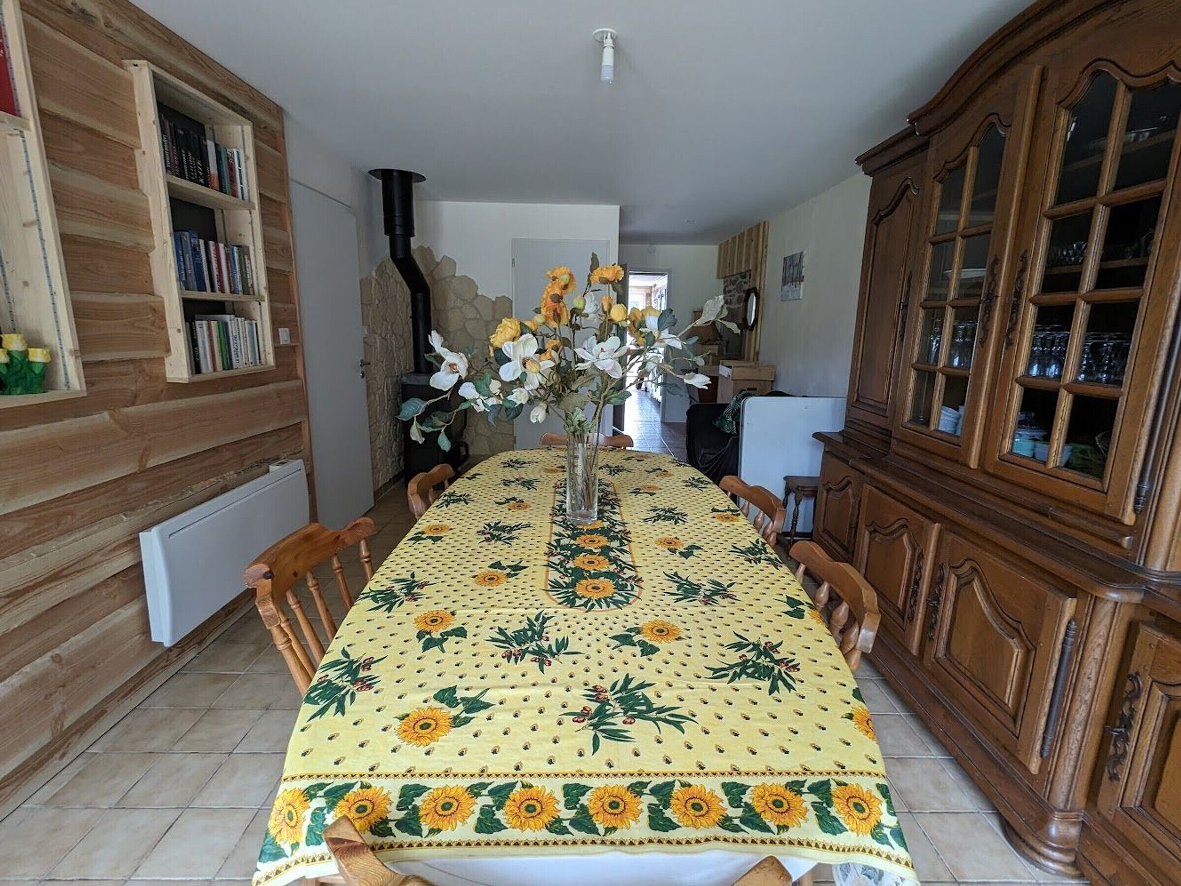 Un coin repas avec une table recouverte d’une nappe à motifs floraux, des chaises en bois et un vase rempli de fleurs.