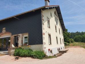 Een gebouw met twee verdiepingen, een zwart dak, beige muren en een stenen fundering.