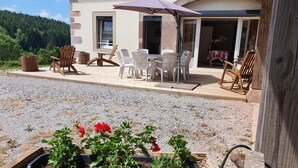 Eine Holzterrasse mit Gartenmöbeln, ein erhöhter Blumenkasten mit Pflanzen und ein Gebäude mit einer Steinaußenfassade.