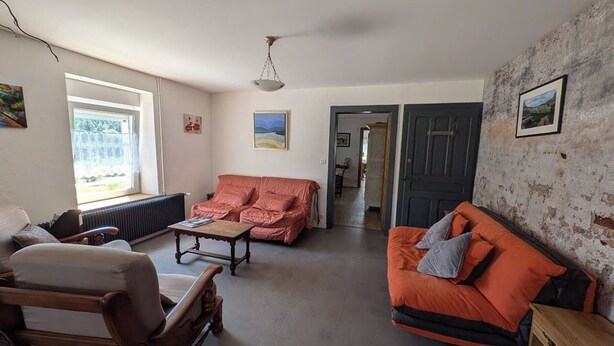 Ein Wohnzimmer mit einer Couch, einem Sessel und einem Couchtisch. Eine Tür führt in einen anderen Raum.