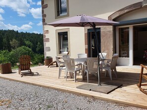 Eine Terrassengruppe mit Tisch und Stühlen, ein Holzstuhl und ein großer Sonnenschirm.