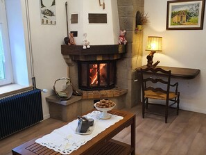 A cozy living room with a fireplace, a table with a tea set, a chair, and a radiator.