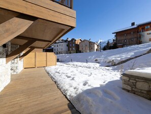 A wooden deck with a stone wall, snow-covered ground, and buildings in the background. - Apartment with parking - 4 guests (Val-d'Isère)