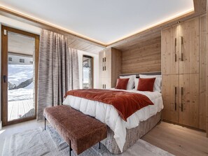 A bedroom with a large bed, a bench, wooden wardrobe, and a view of a snowy landscape. - Apartment with parking - 4 guests (Val-d'Isère)