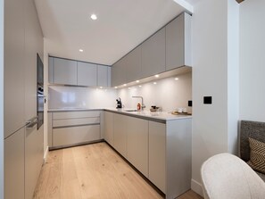 A modern kitchen with built-in appliances, a wooden floor, and a seating area with a sofa and a patterned cushion. - Apartment with parking - 4 guests (Val-d'Isère)