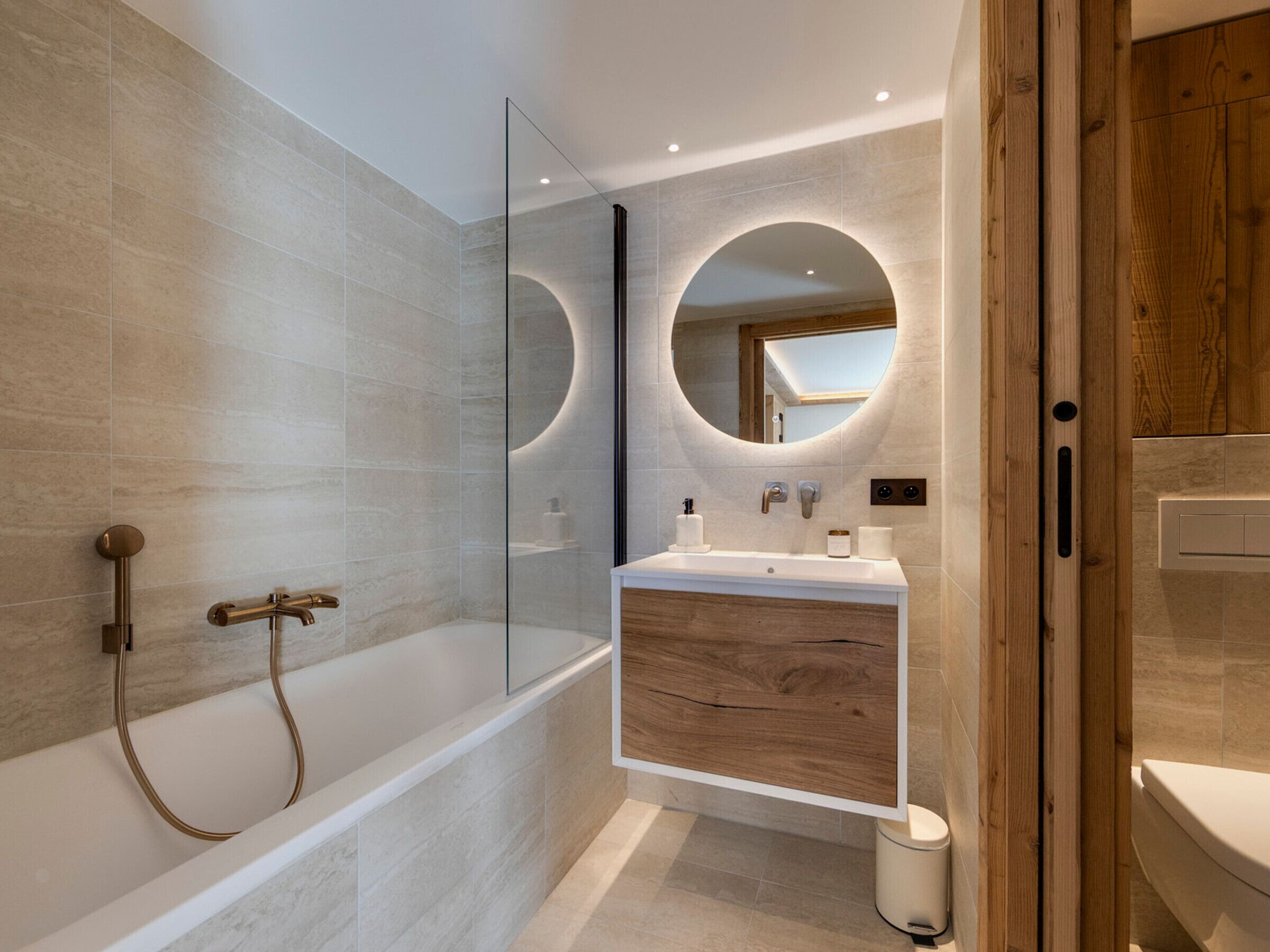 Ein modernes Badezimmer mit einer gläsernen Dusche, einem Holzkosmetikschrank und einem großen Spiegel.