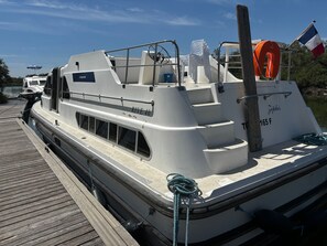 A white boat docked at a pier with a lifebuoy and a flag. - Spacious houseboat at the port - 8 guests (Mauguio)