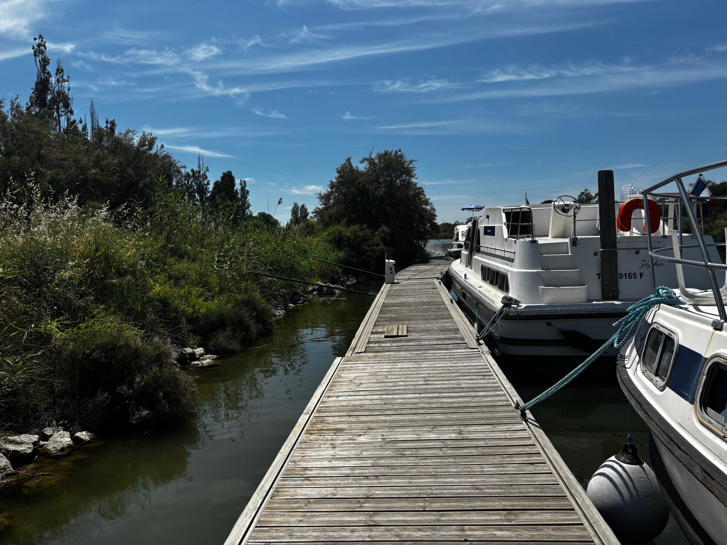 A wooden dock extending into a calm river, with a boat docked on the right.