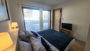 Ein Hotelzimmer mit Bett, Fernseher, Lampe und einer Glastür, die zu einer verschneiten Außenanlage führt.