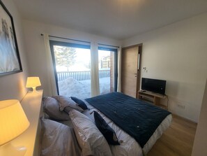 Ein Hotelzimmer mit Bett, Fernseher, Lampe und einer Glastür, die zu einer verschneiten Außenanlage führt.