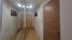 Ein Flur mit Holzboden, weißen Wänden und einer Holztür. Deckenleuchten und gerahmte Bilder schmücken die Wände.