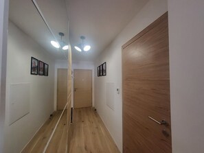 Ein Flur mit Holzboden, weißen Wänden und einer Holztür. Deckenleuchten und gerahmte Bilder schmücken die Wände.