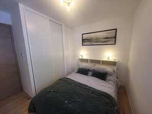 Ein Schlafzimmer mit Bett, Nachttischlampen, einem Kleiderschrank und einem gerahmten Bild an der Wand.