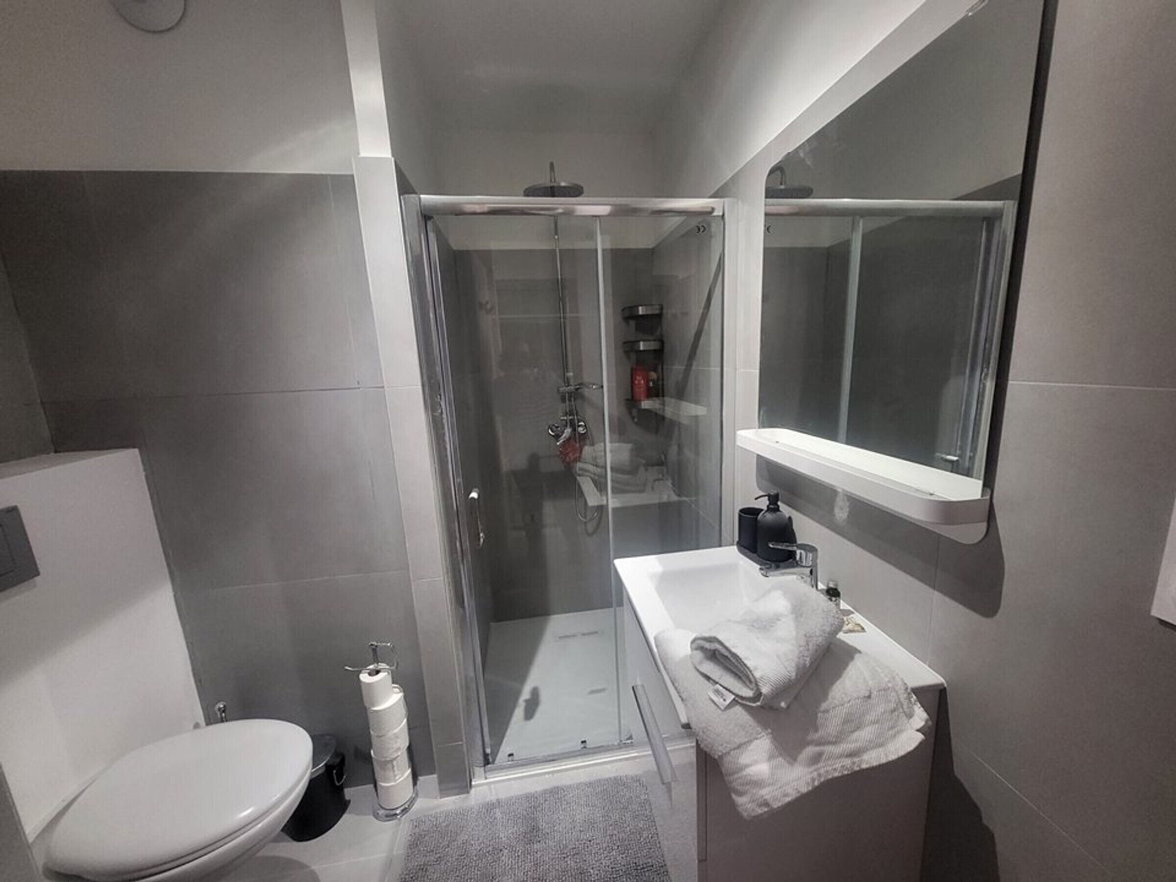 Un baño pequeño con inodoro, ducha con mampara de vidrio y lavamanos con toalla.