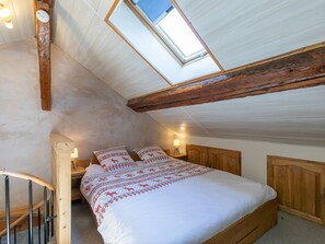 Ein Schlafzimmer mit Oberlicht, Holzbalken, einem Bett mit gemusterten Betttextilien und einem hölzernen Kopfteil.