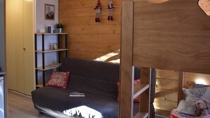 Ein Zimmer mit einem Etagenbett, einer Schlafcouch, einer Holzwand und einem Regal mit Gegenständen.