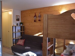 A room with a bunk bed, a sofa, a wooden wall, and a shelf with items. - Central studio in Montgenèvre - 2 guests (Montgenèvre)